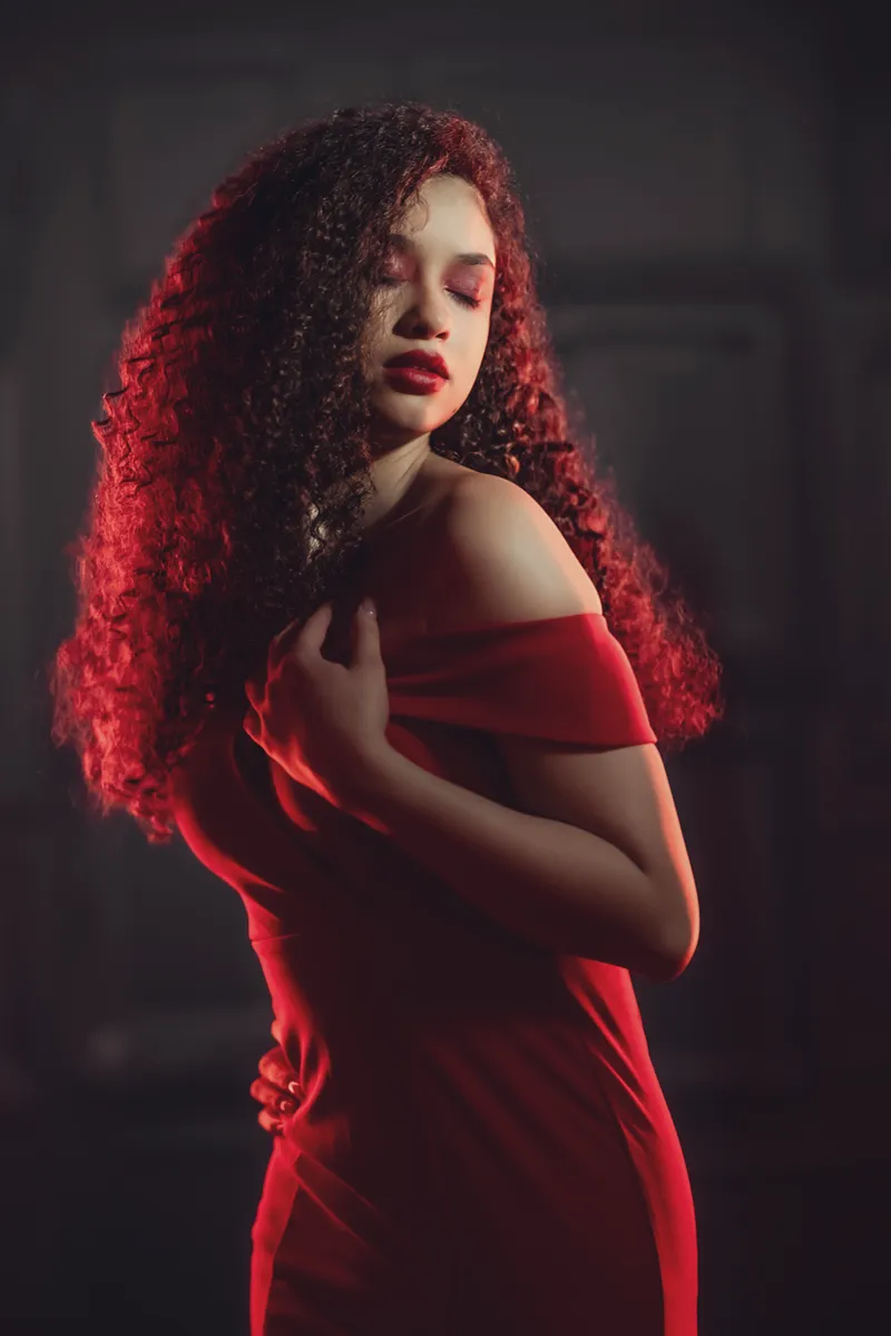Studio photo of model looking over her left shoulder, eyes close wearing a red dress